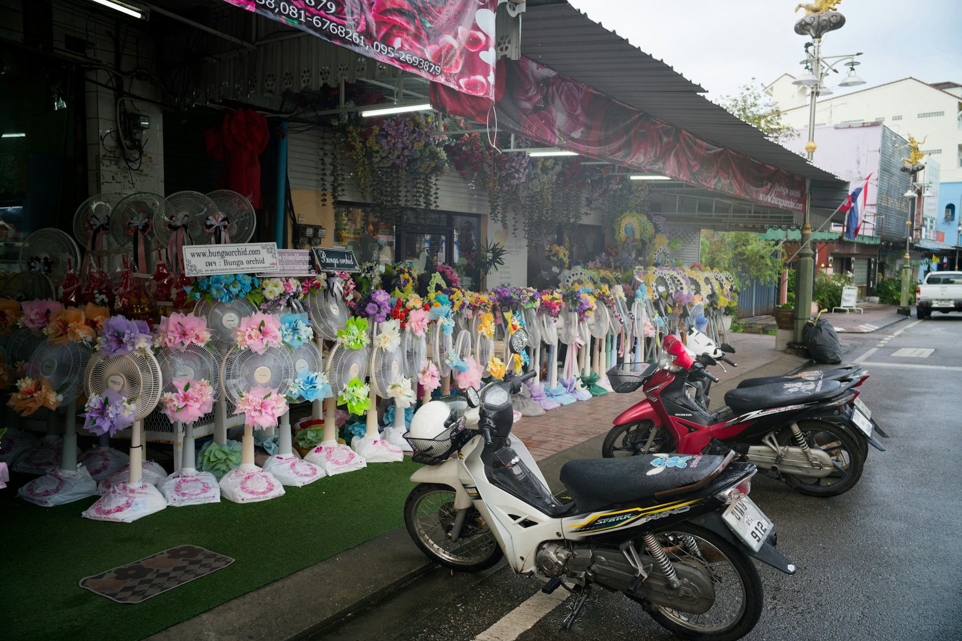 Storefront with fans and flowers, motorcycles parked outside.